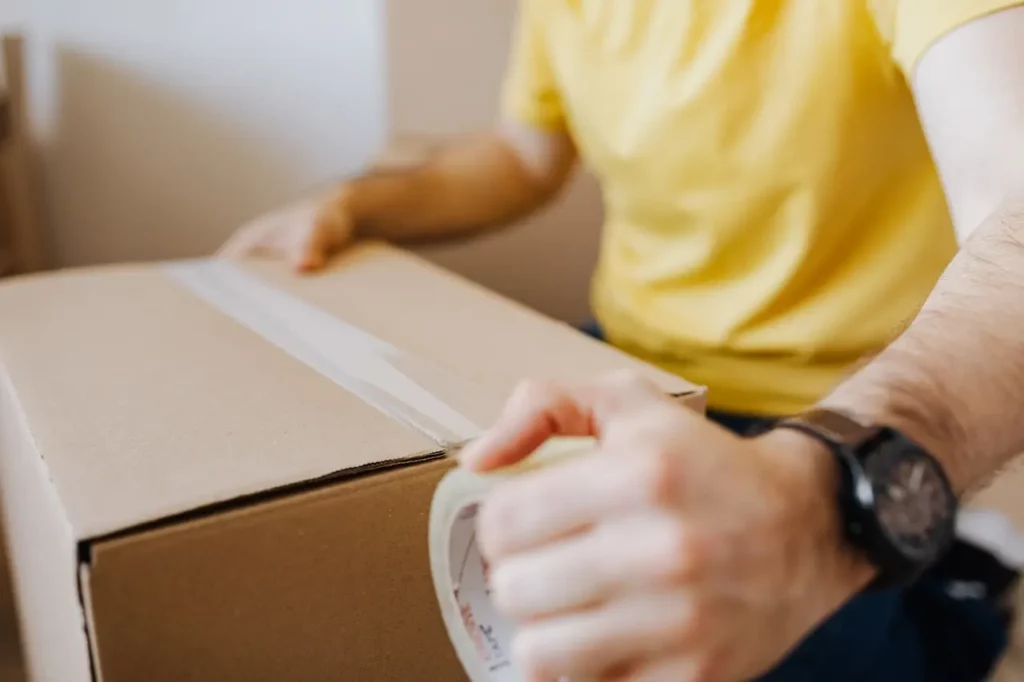 Man taping up a cardboard storage box, as if he is moving out of the house