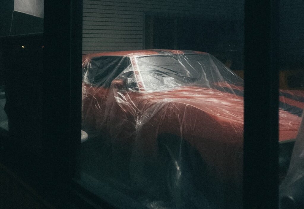 A car in a garage under a plastic cover.