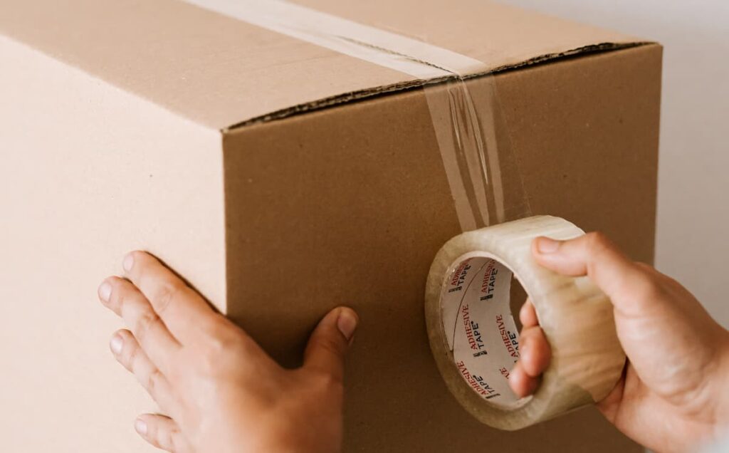 A person seals a cardboard box with packing tape.